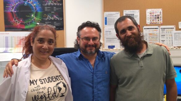 Three scientists pose together in a laboratory with computers and research materials.
